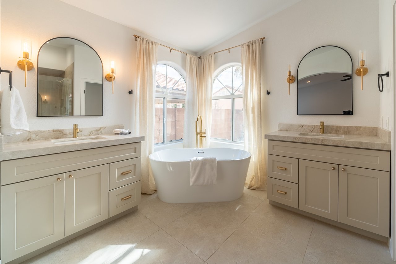 Bathroom with a freestanding tub between matching vanities and tall arched windows.