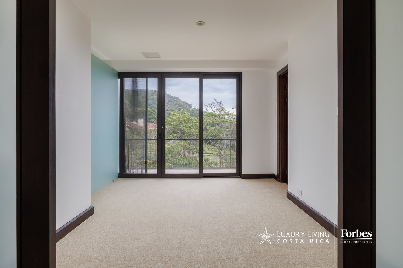 Empty carpeted room with sliding glass doors opening to a balcony and hillside views.