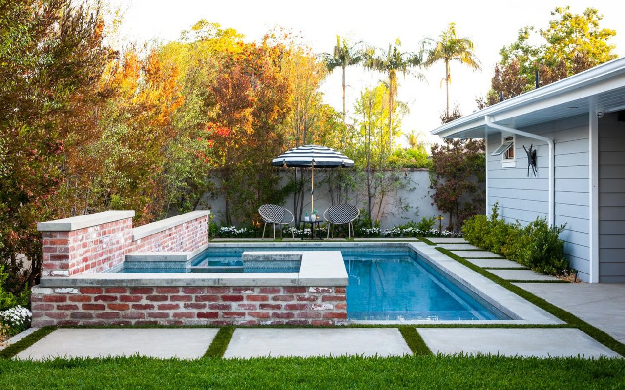 A home in Newport Beach with a swimming pool, an adjacent spa with brick accents, and a striped umbrella over two chairs.