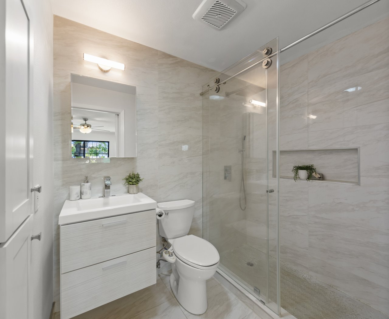 Bathroom with marble-look tile, a white vanity, and a glass walk-in shower.