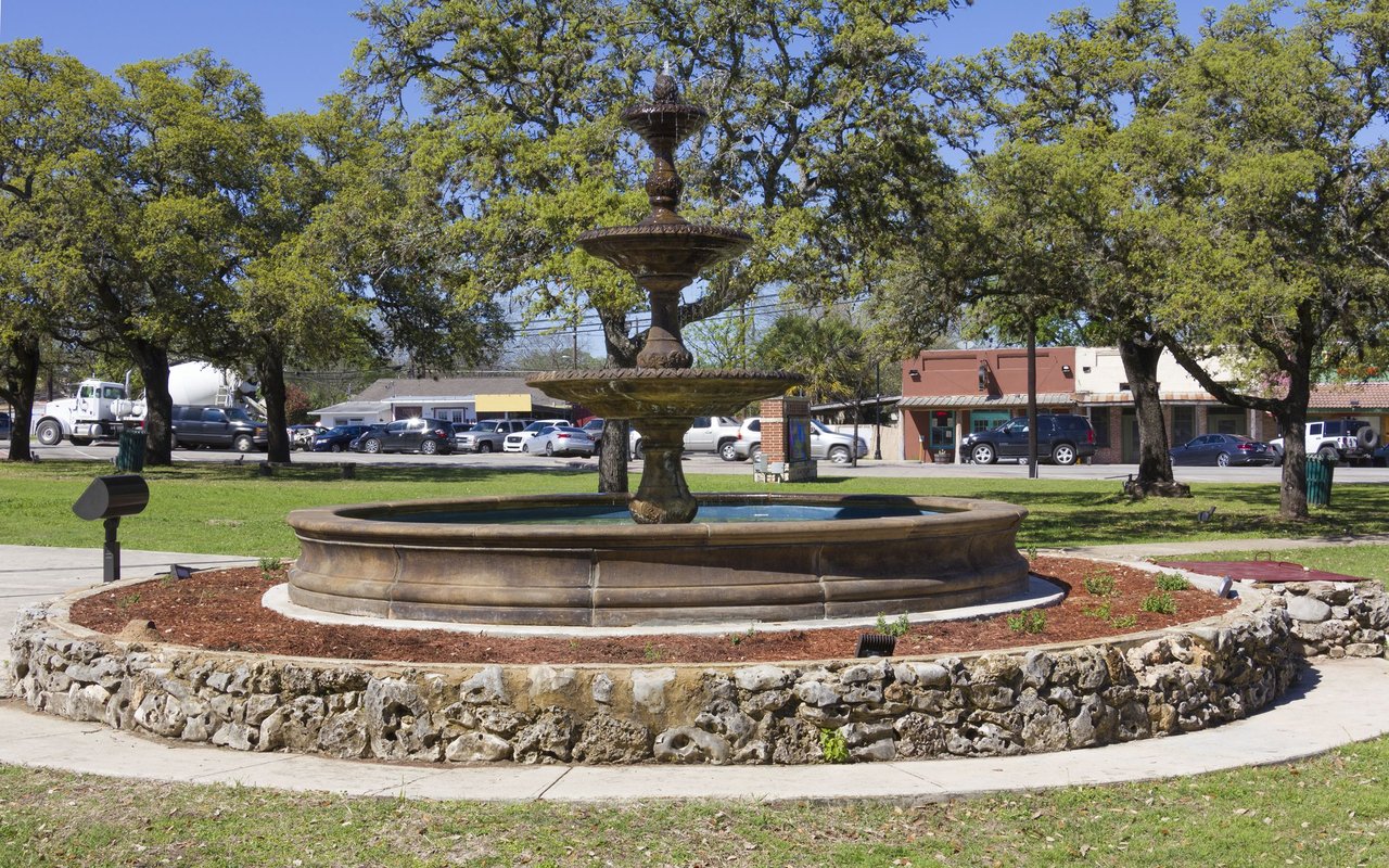 Tiered stone fountain in Kyle, surrounded by mature oak trees.