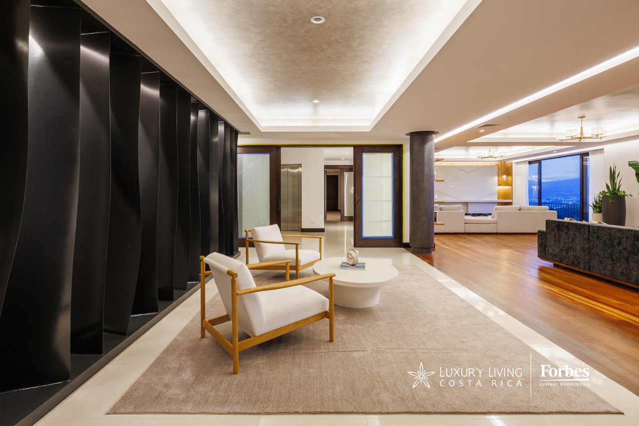 Penthouse living room with white armchairs, dramatic black wall panels, and city views through wide windows.