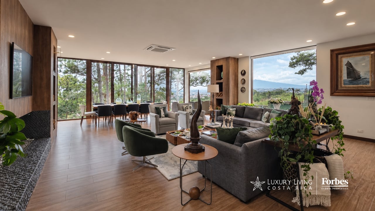Open-plan living and dining room with floor-to-ceiling windows, a fireplace, and distant hills.