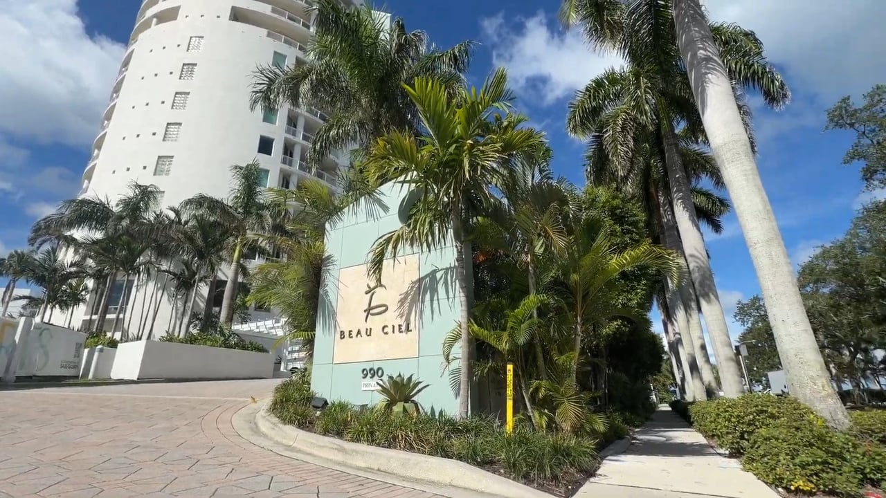 Beau Ciel condominium entrance with a white high-rise, palm trees, and landscaped grounds.