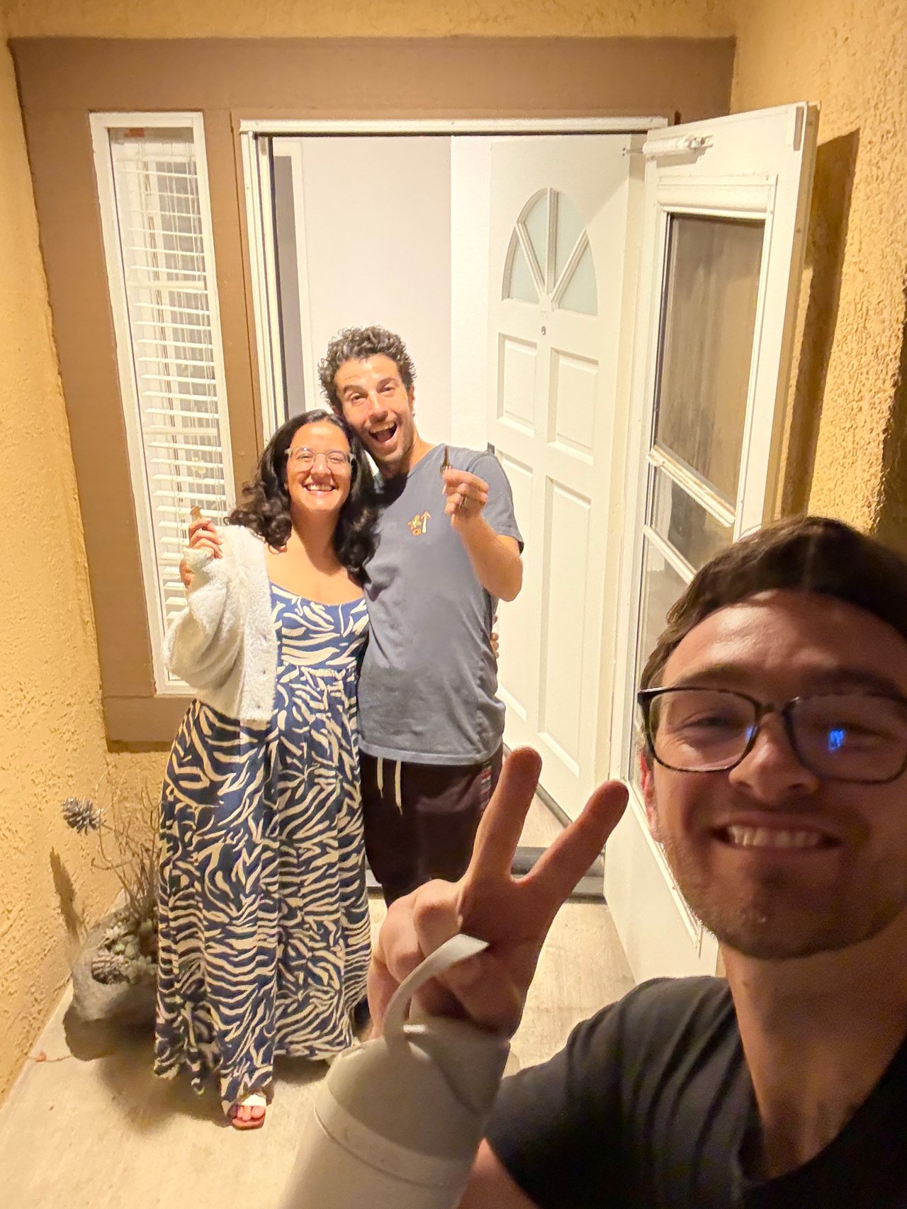 Real estate agent takes a selfie with a smiling couple holding a key at their front door.