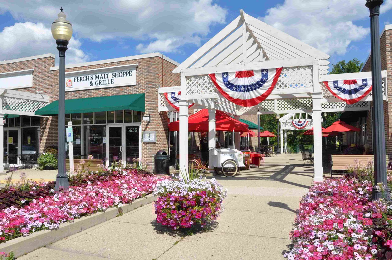 Downtown Greendale with Ferch’s Malt Shoppe, outdoor seating, white pergola, and vibrant summer flowers.