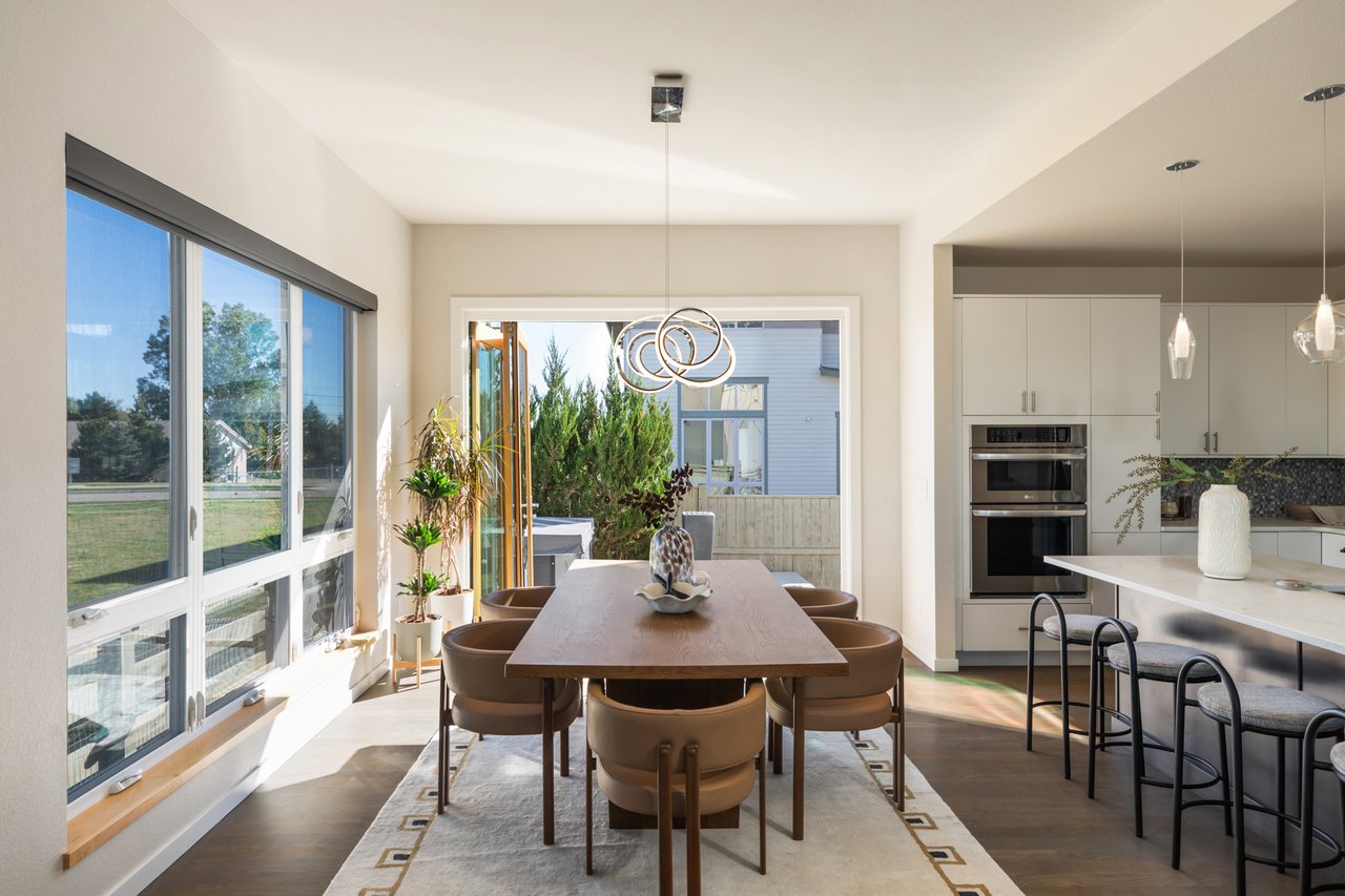 Dining area with a wood table and pendant lights beside open accordion doors leading to the back patio