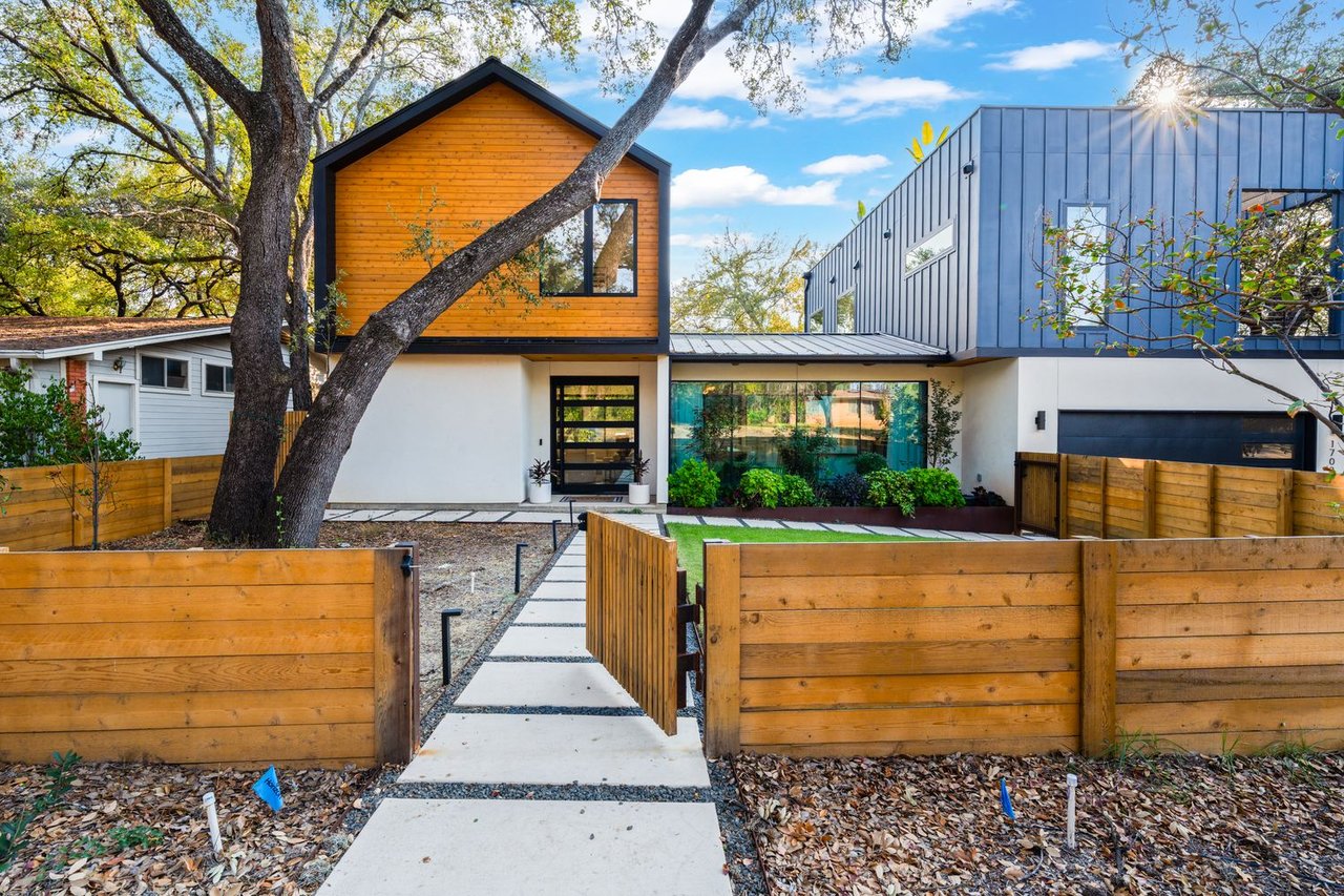 Modern two-story home with wood and blue-gray metal siding, an oak tree, and a wooden front fence.