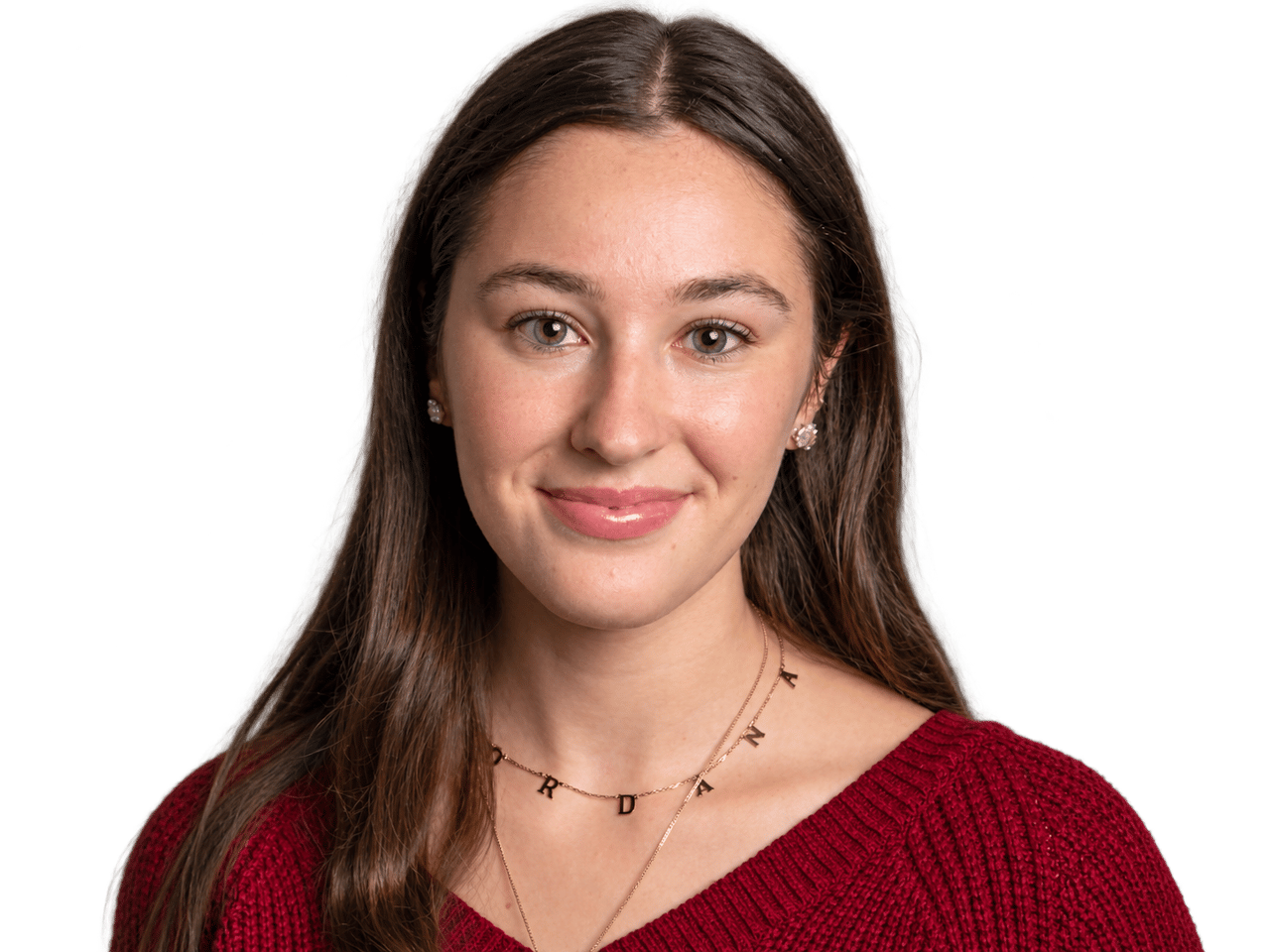 Jordana Marks with long brown hair, wearing a red sweater and gold necklaces.