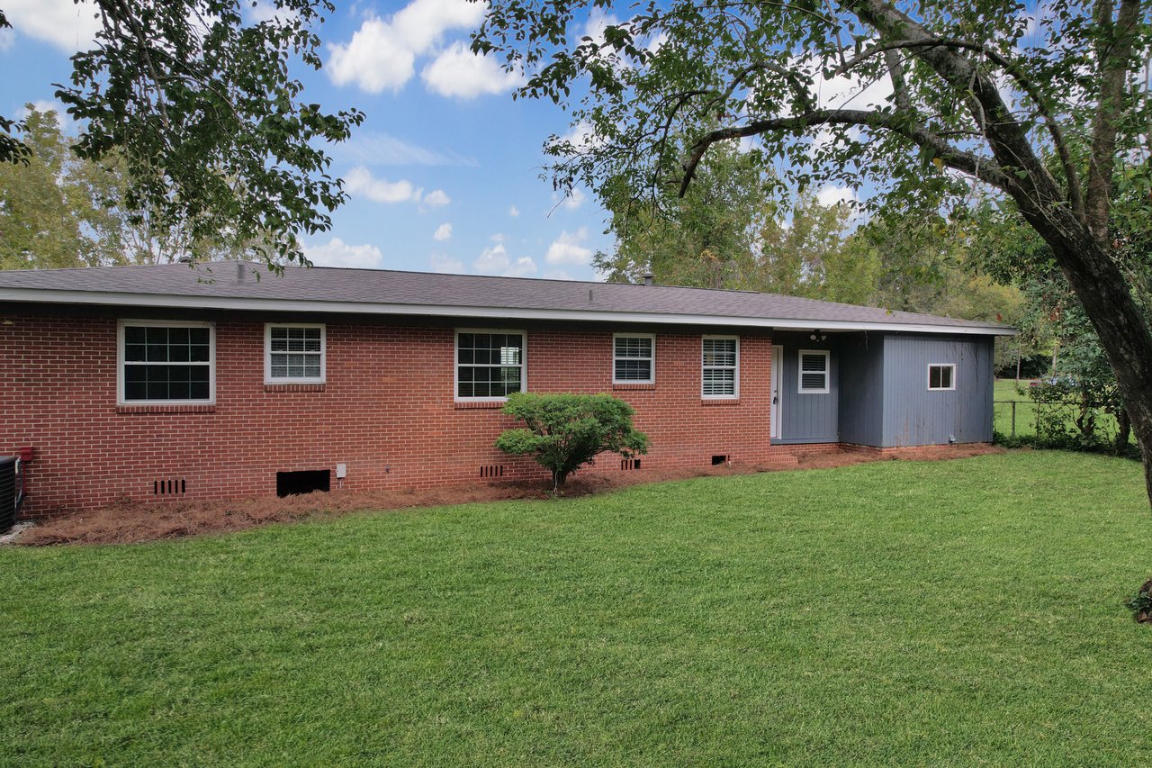 A brick home surrounded by a lush yard and trees, showcasing a serene and inviting outdoor environment.