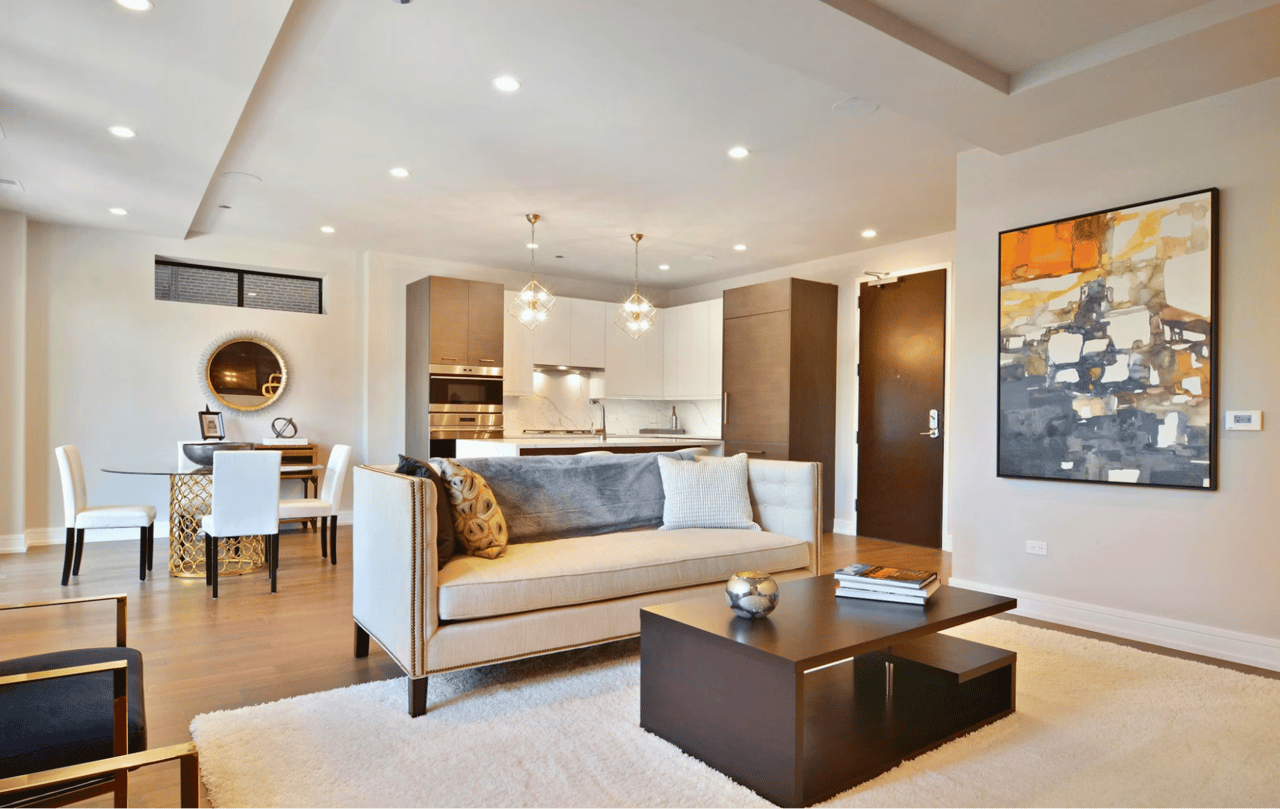 Furnished condo living room with an open kitchen, hardwood floors, and a large abstract painting.
