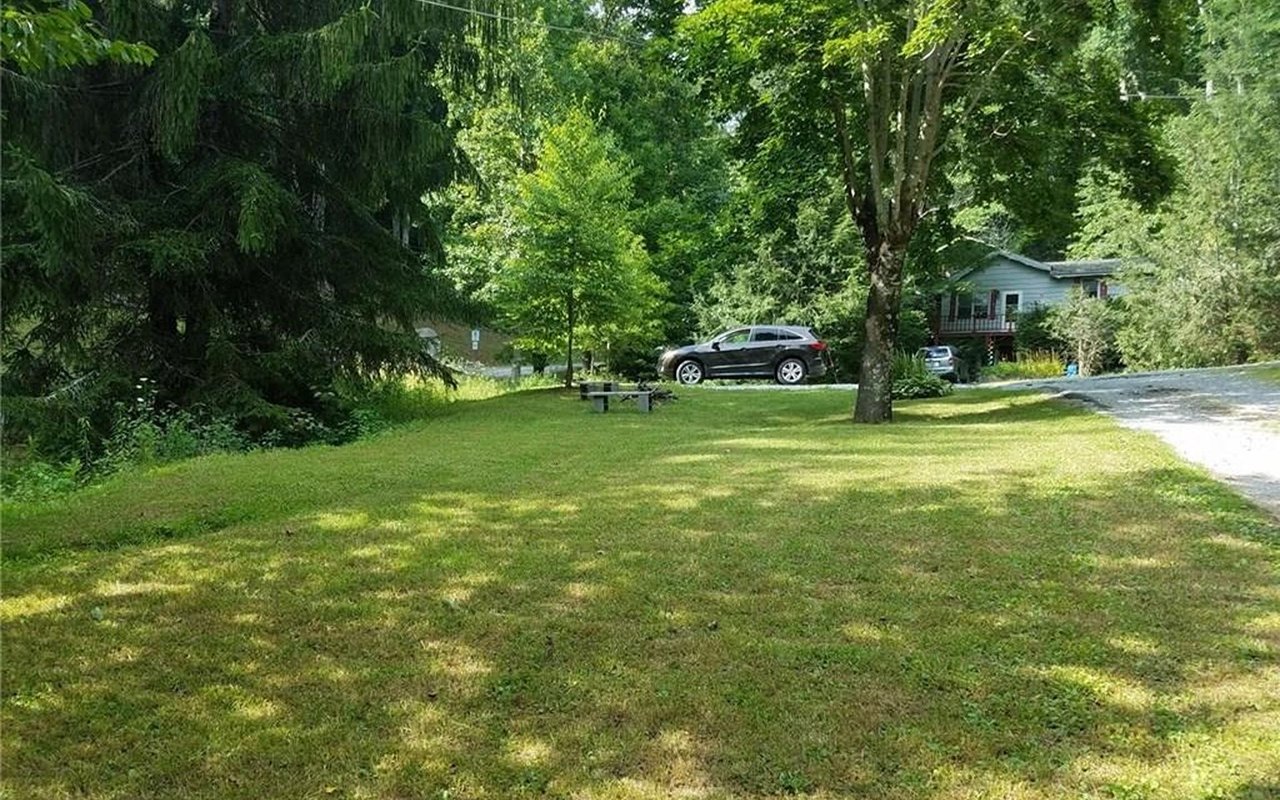 House among trees beyond a broad lawn, with a gravel driveway and raised deck.