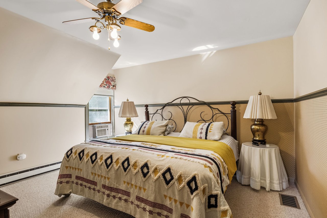 Bedroom with patterned cream and yellow bedding, an ornate metal headboard, and a ceiling fan.