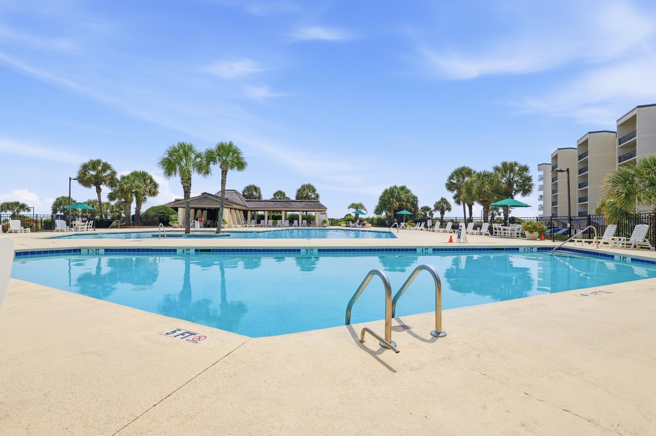 Heron Marsh Villas outdoor pool with palm trees, a pavilion, and condominium buildings.