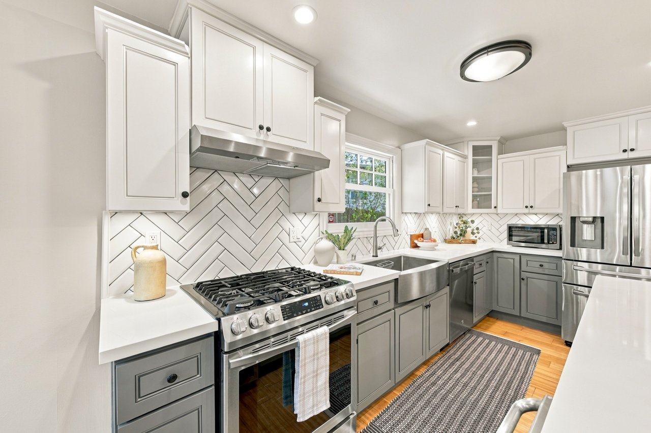 Kitchen with gray lower cabinets, herringbone tile backsplash, stainless-steel range, and farmhouse sink.