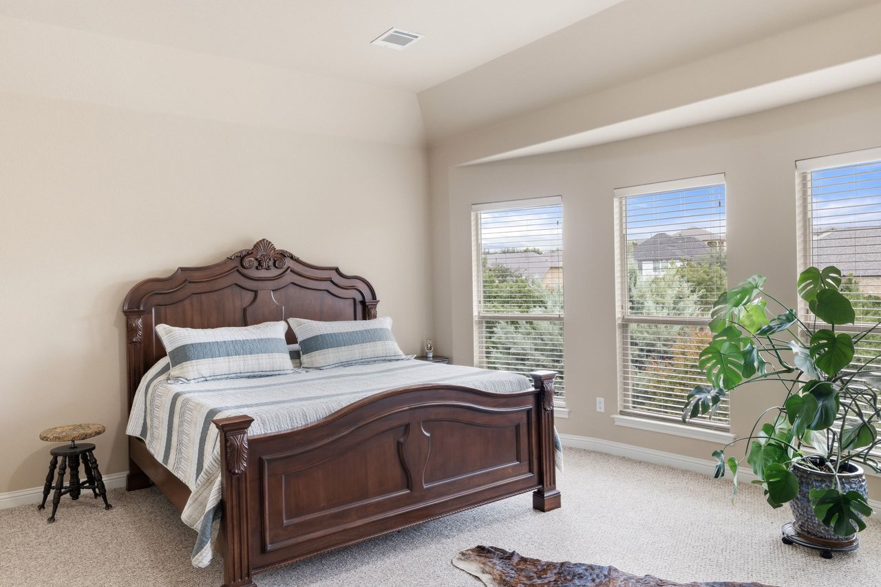 Bedroom with a carved wooden bed, striped bedding, and three large windows.