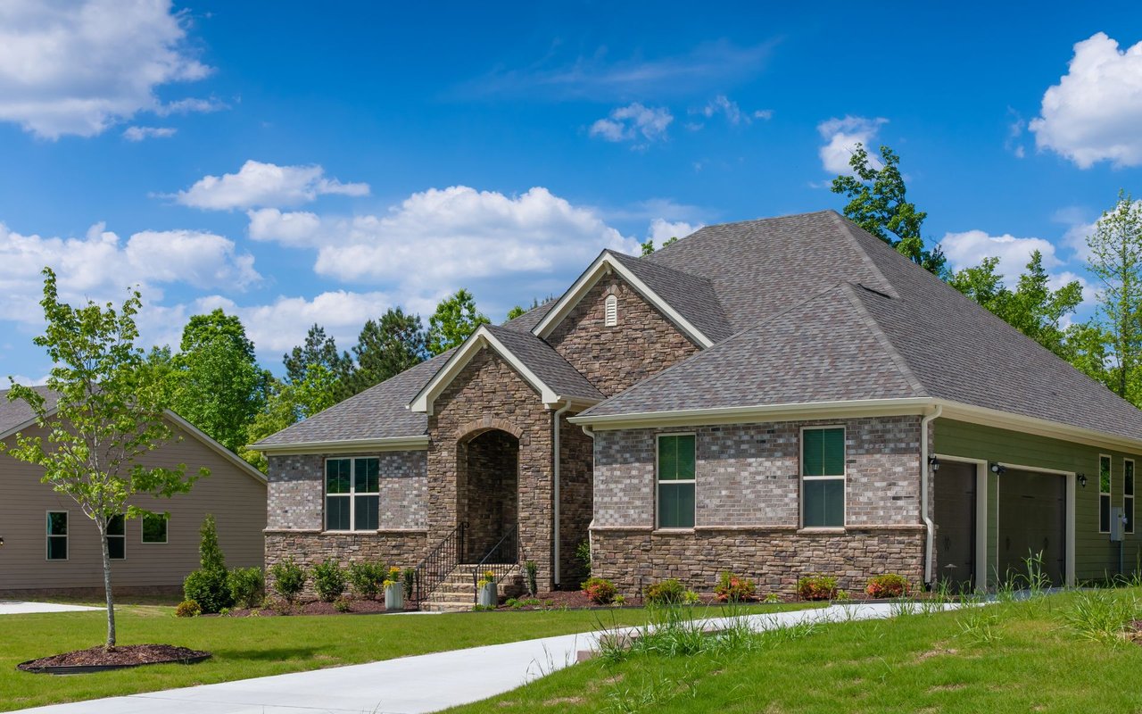 Stone-and-brick home with an attached garage, landscaped lawn, and concrete driveway.
