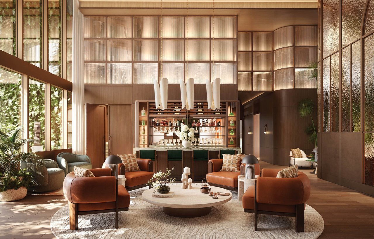 The Well’s double-height lounge with a central bar, rust-colored chairs, and tall windows facing greenery.
