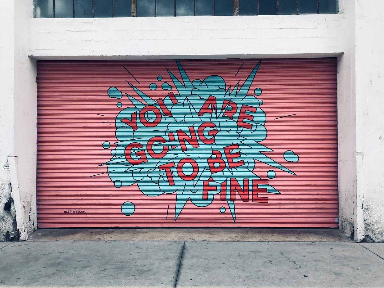 Pink roll-up garage door with a teal comic-style burst reading “YOU ARE GOING TO BE FINE."