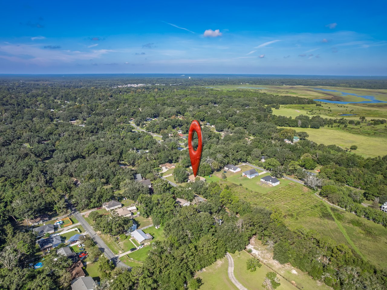 Aerial view of a wooded neighborhood and wetlands, with a red marker identifying the property.
