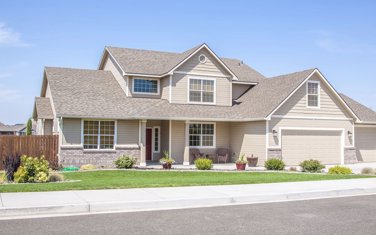 Two-story beige house with brick accents, a two-car garage, and a landscaped front lawn.