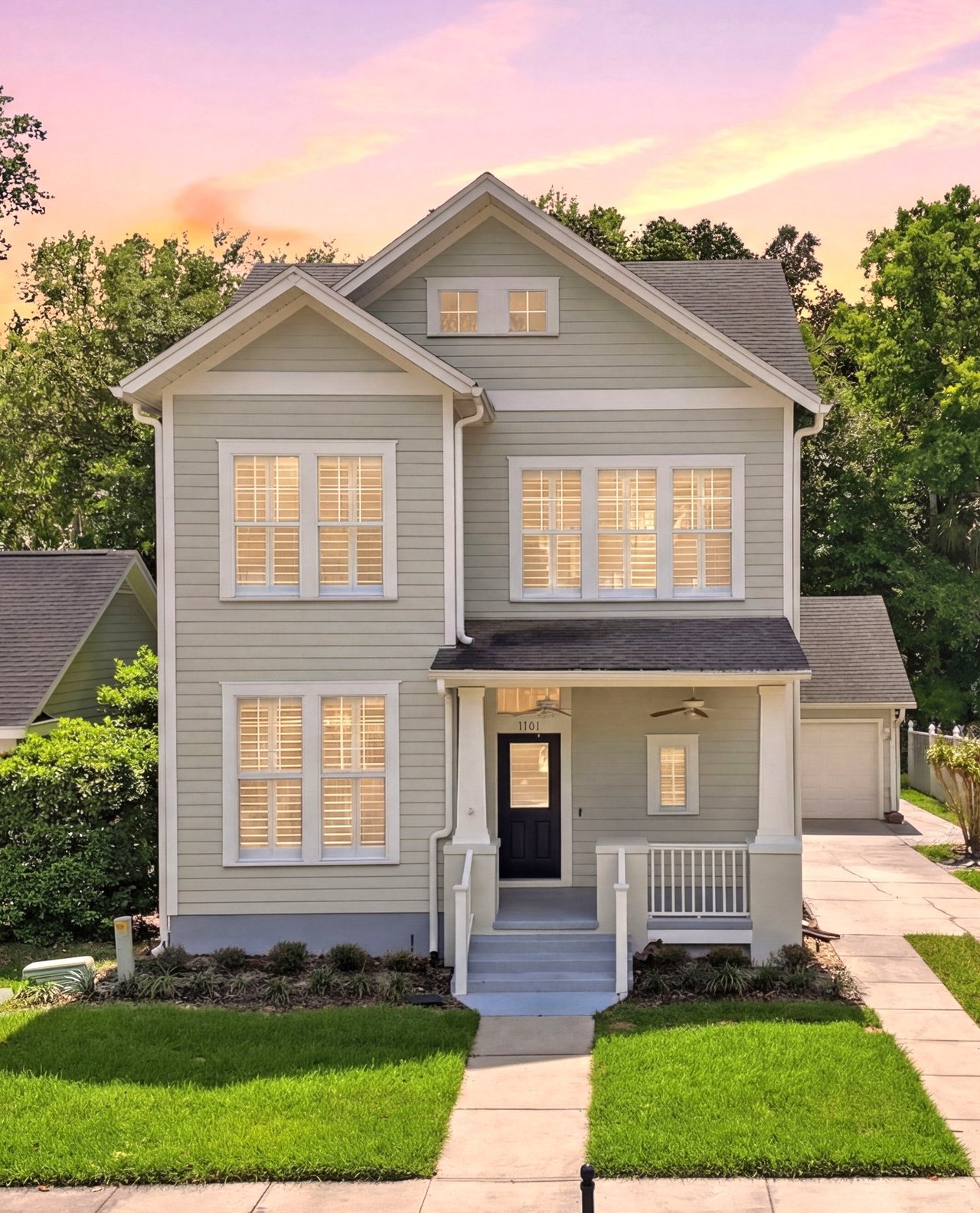 Two-story gray-green house with white trim and a covered porch at sunset.