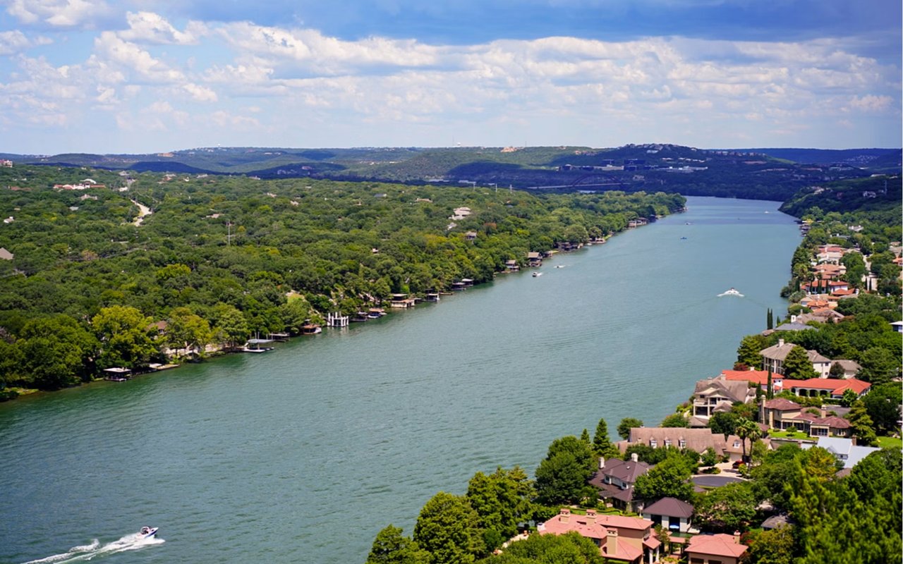 Aerial view of a lake bordered by wooded hills and waterfront homes, with boats on the water.