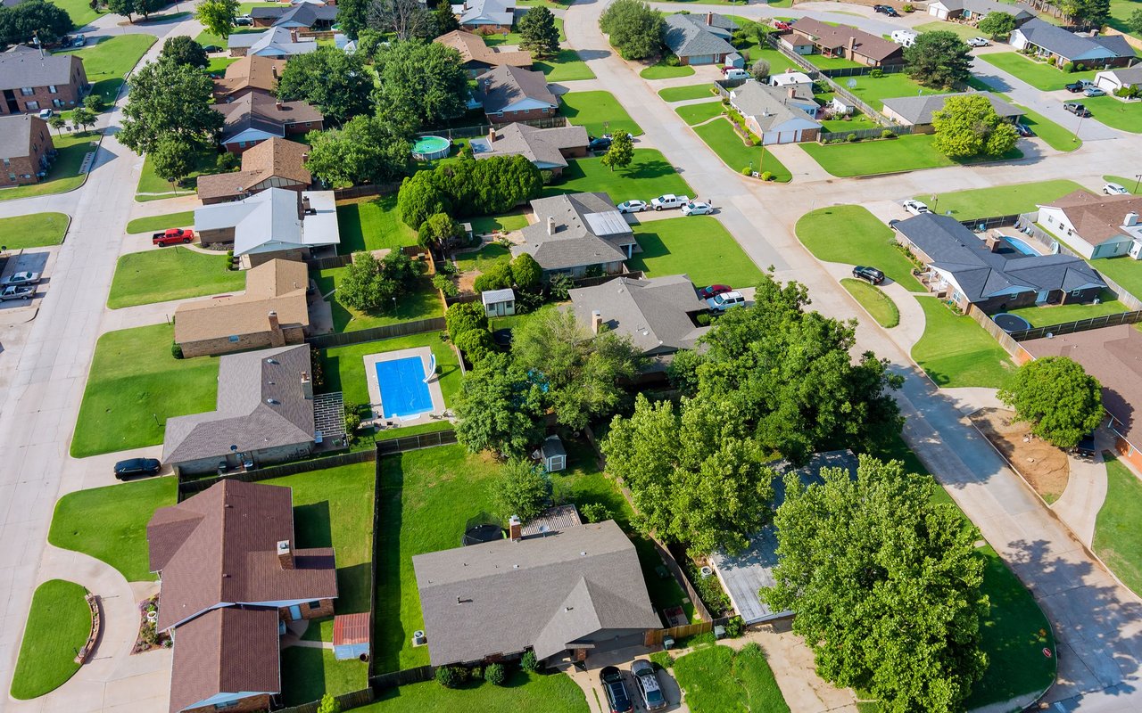 Aerial view of a leafy neighborhood with detached homes, curved streets, and backyard pools.