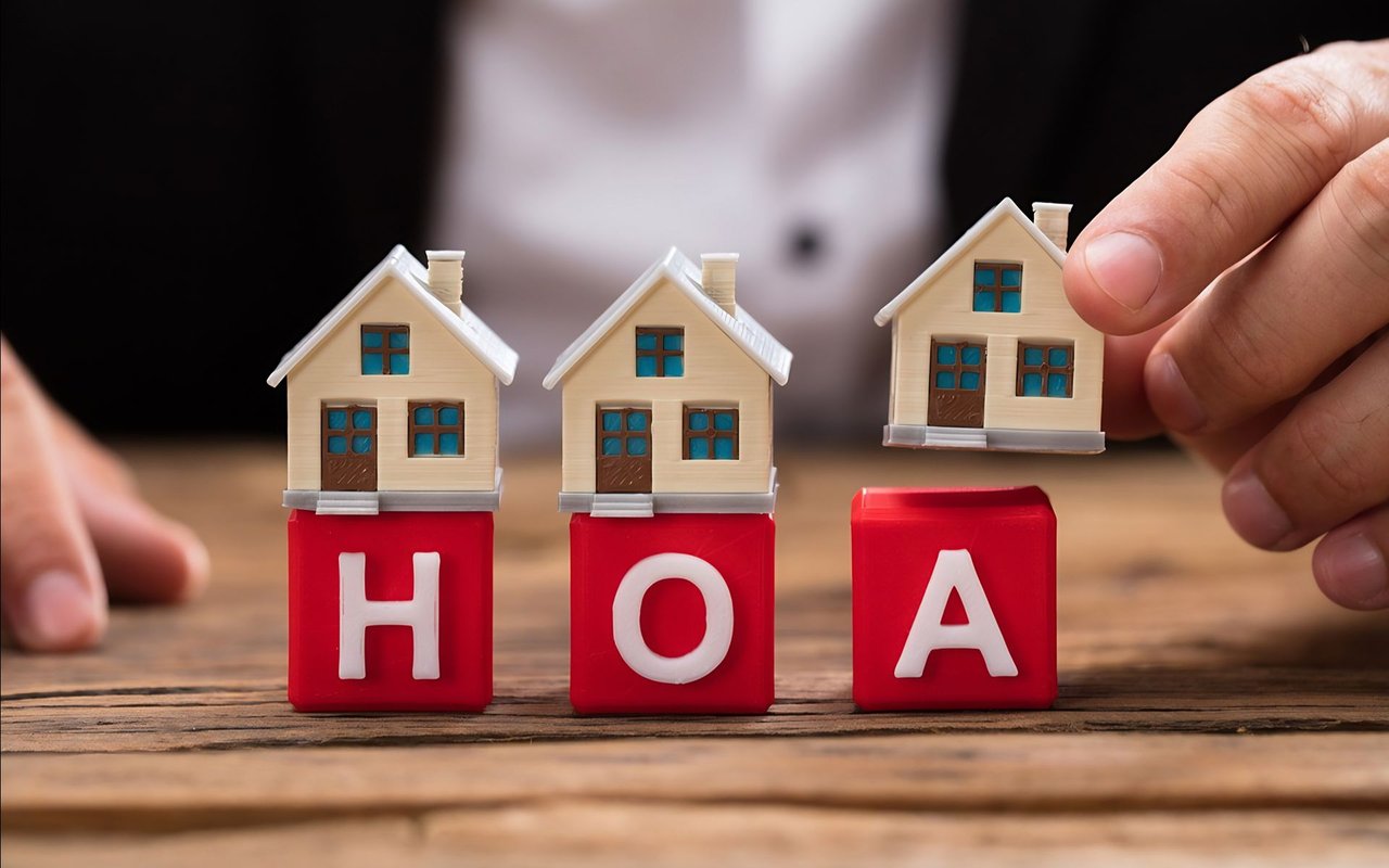 Miniature houses on red blocks spelling HOA as a hand lifts one house.
