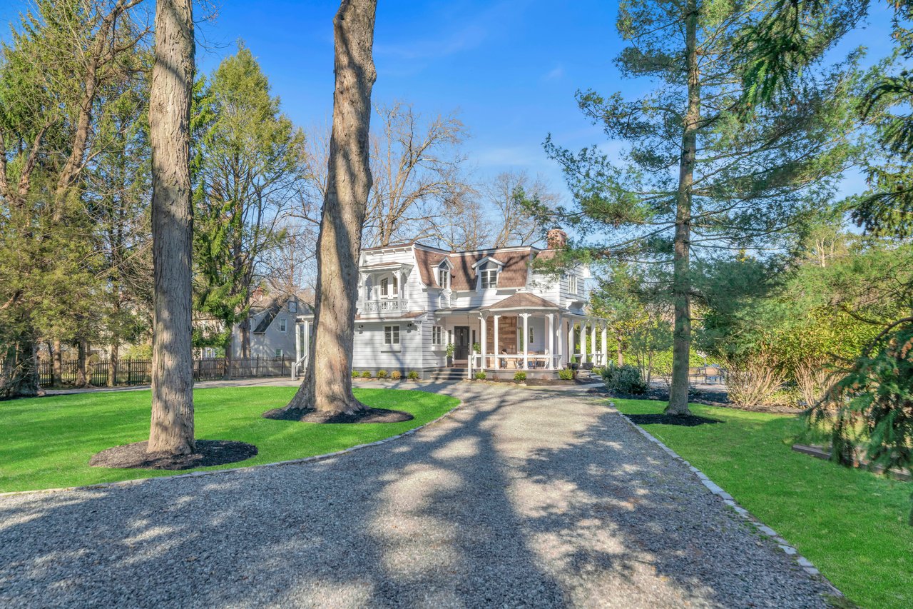 Front exterior view of a private retreat home with a circular gravel driveway and lush lawn in Harrington Park, NJ