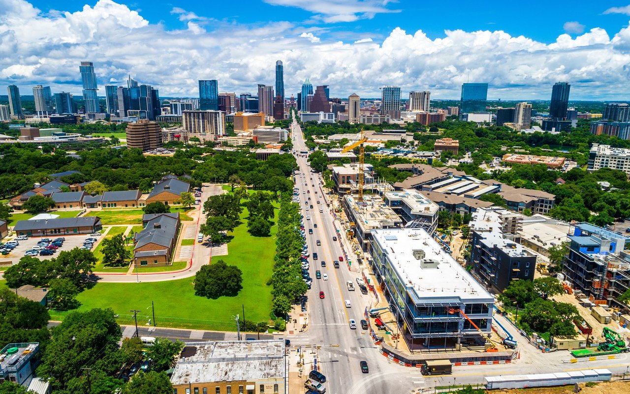 Aerial view of downtown Austin with a broad road, green space, and construction in the foreground.