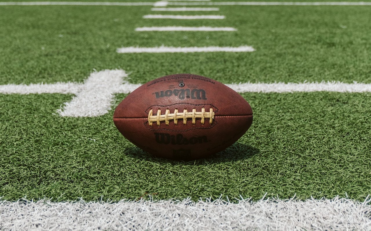 Wilson football on green turf beside a white field marking.