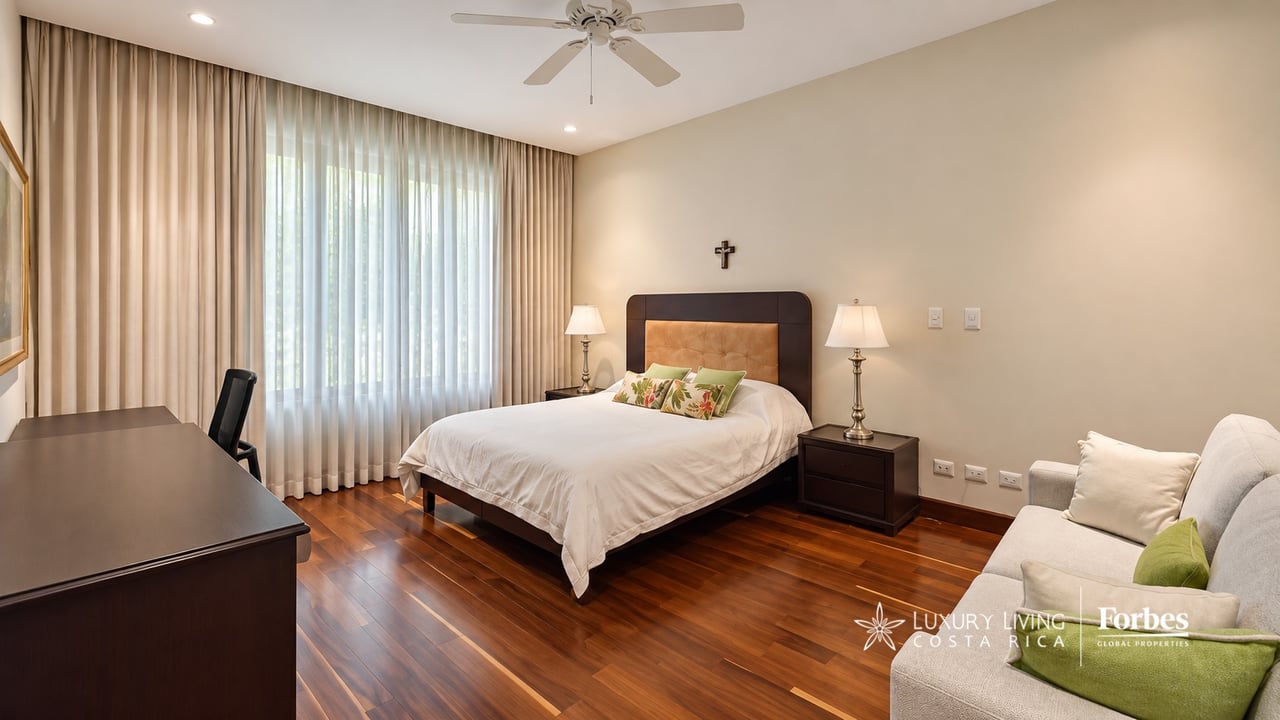 Furnished bedroom with a large bed, wood floors, desk, and sofa seating area.