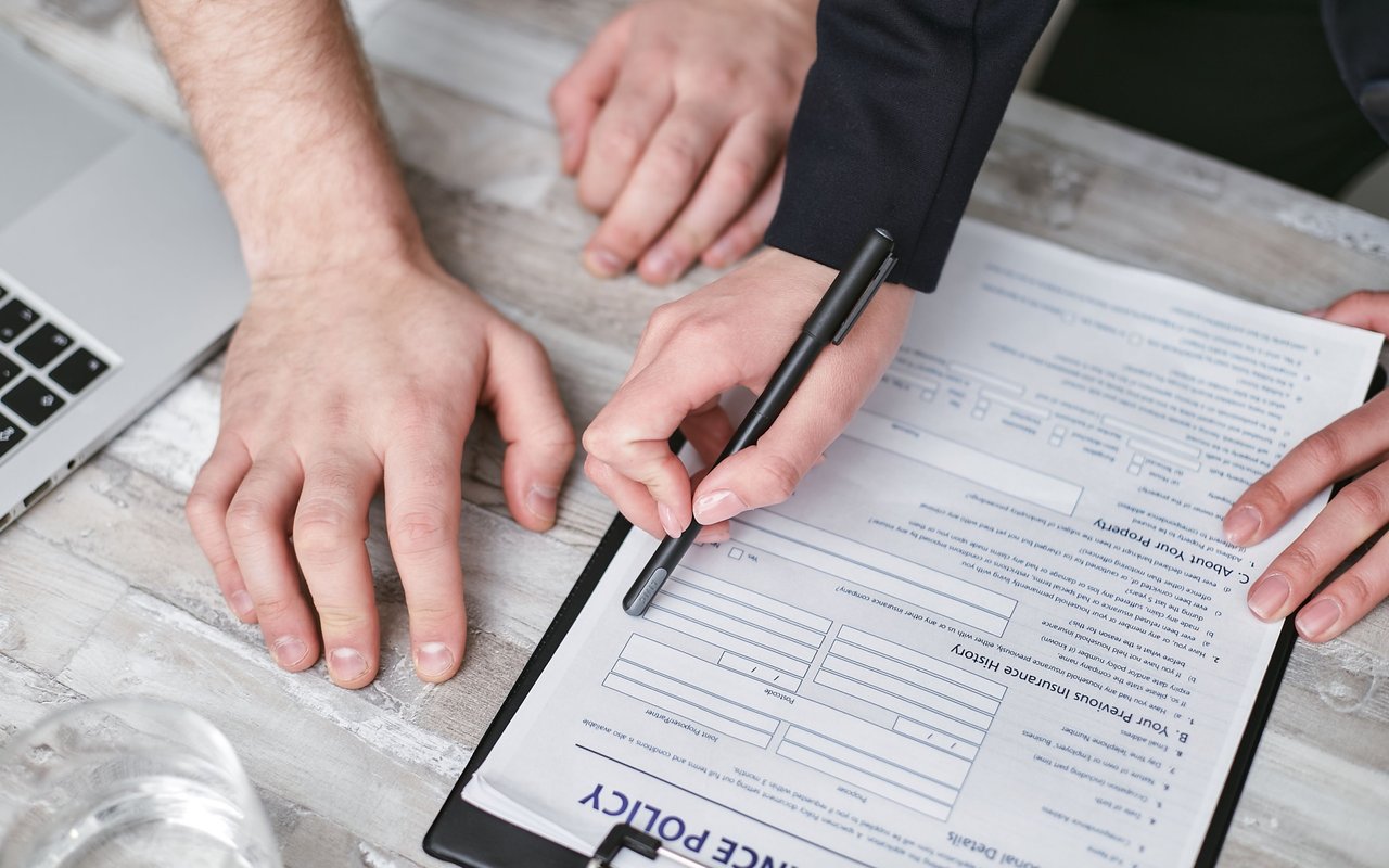 Hands signing a title insurance policy beside a laptop.