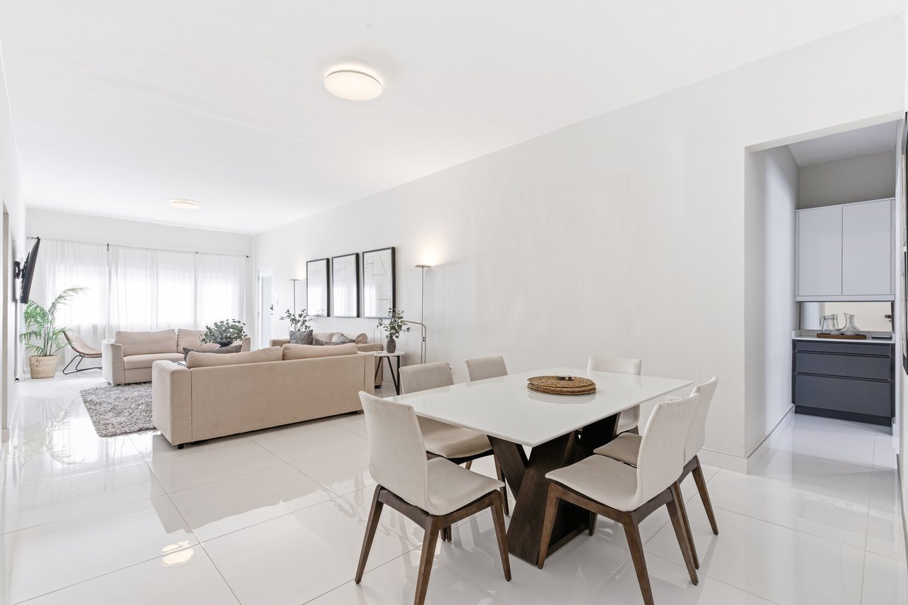 Open-plan living and dining room with neutral sofas, a white dining table, and a kitchen nook.