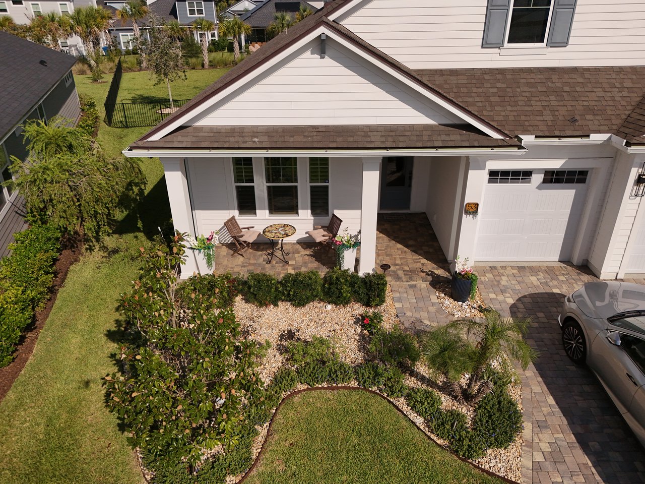 Home with a covered porch, attached garage, and curved landscaped garden beds, viewed from above.