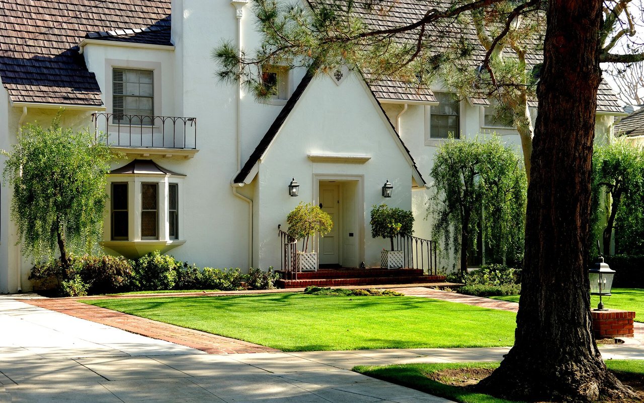 White stucco house with a steep gabled entry, balcony, and landscaped front lawn.