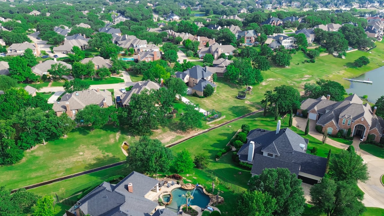 Aerial view of a leafy neighborhood with detached homes, spacious lawns, and a swimming pool.
