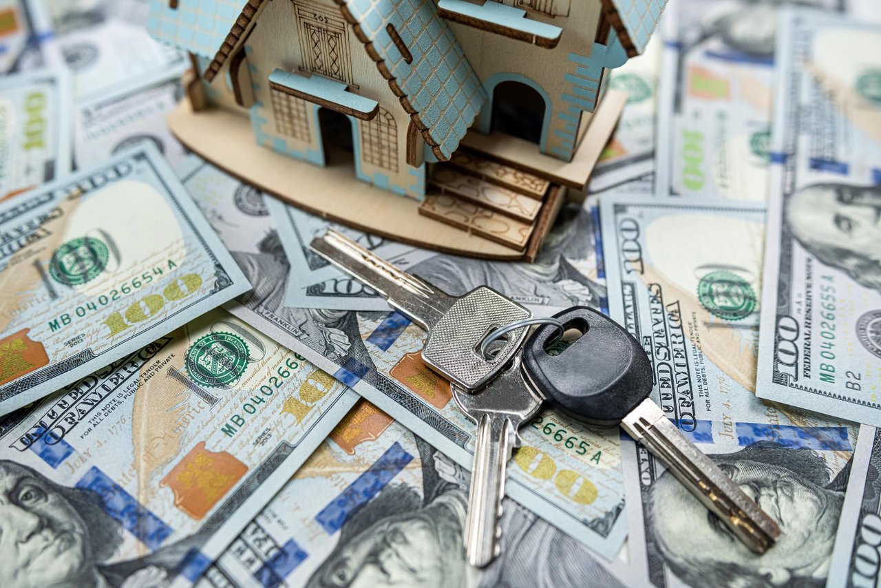 Set of house keys on top of $100 bills next to a miniature wooden house, representing home value and real estate sales in Houston.