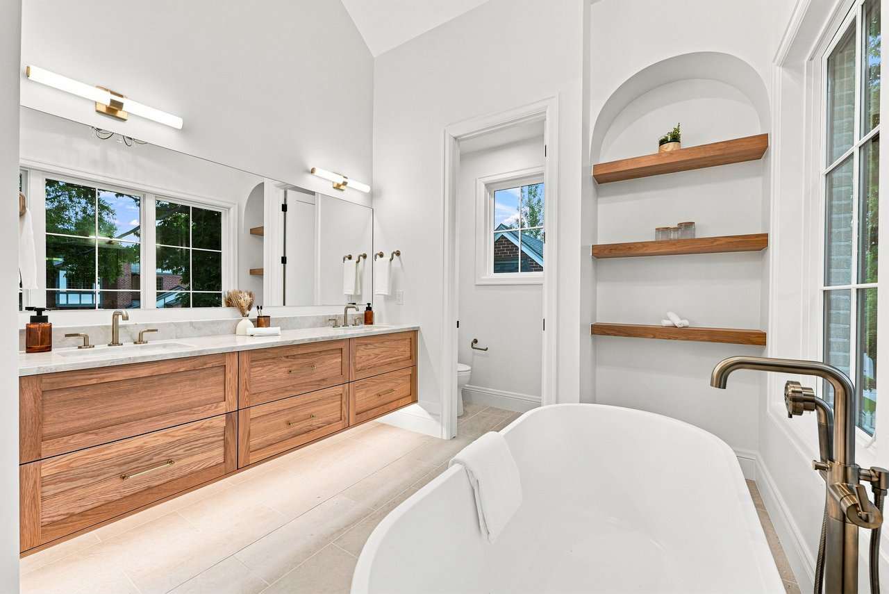 Bright bathroom with a freestanding tub, double wood vanity, and arched built-in shelves.