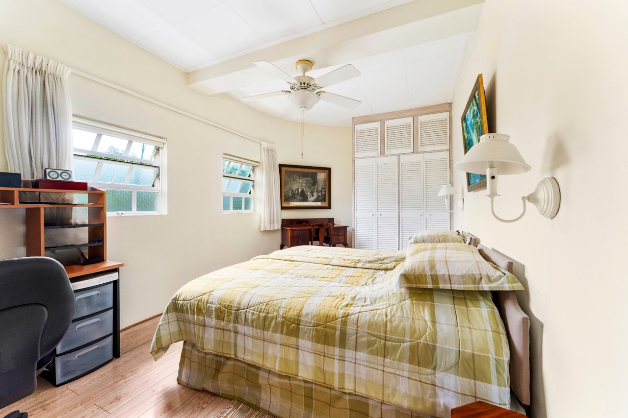 Bedroom with yellow plaid bedding, louvered closet doors, and curtained windows.