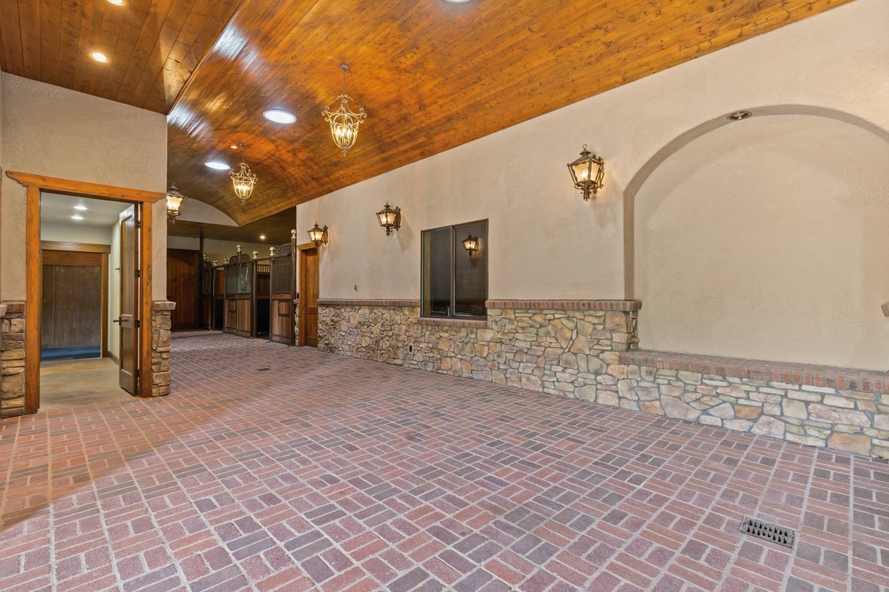 Equestrian barn interior with brick flooring, stone walls, and a vaulted wood ceiling.