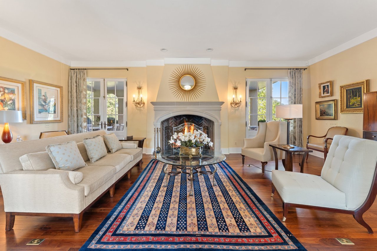 Living room with a large fireplace, cream seating, French doors, and a blue patterned rug.
