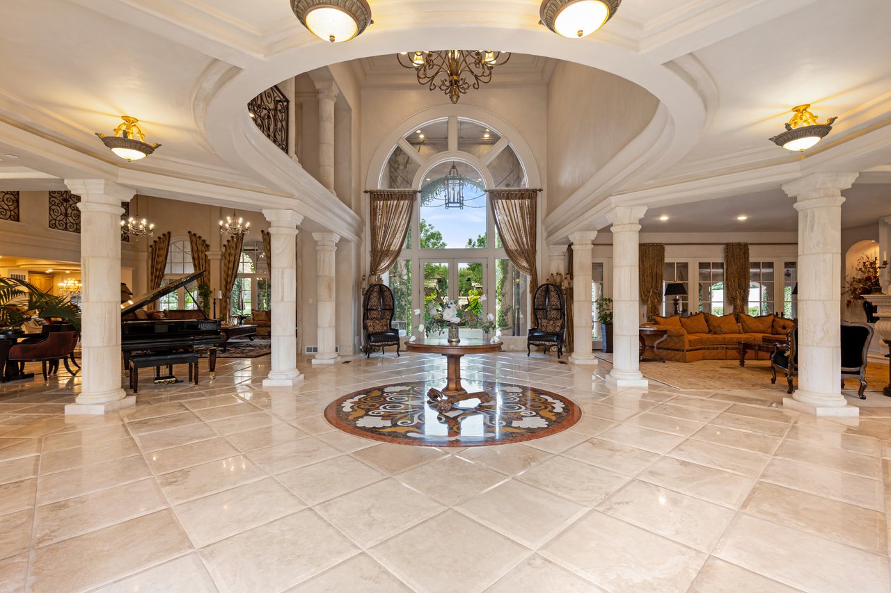 Grand home foyer with marble columns, a tall arched window, and a circular floor medallion.