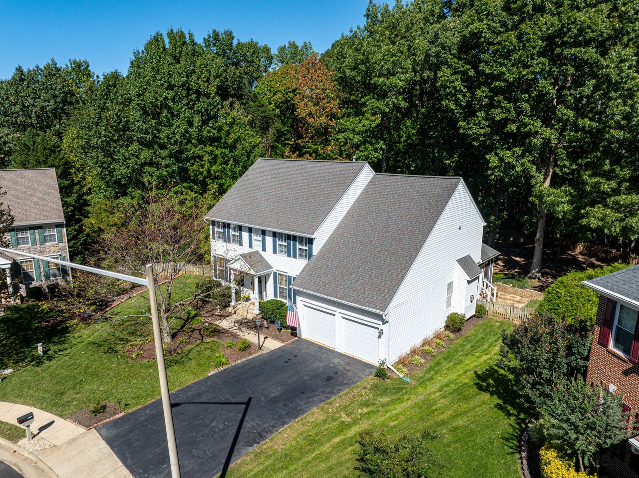 Aerial view of a white two-story house with a double garage, long driveway, and wooded backyard.