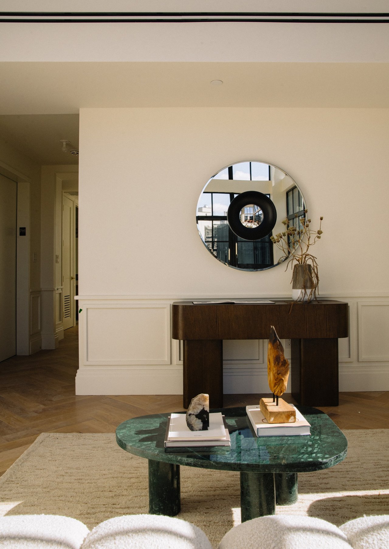 Furnished interior with a round mirror, dark wood console, and green stone coffee table.