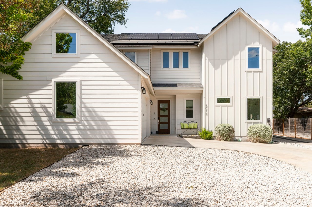 White two-story house with rooftop solar panels and a broad gravel driveway.