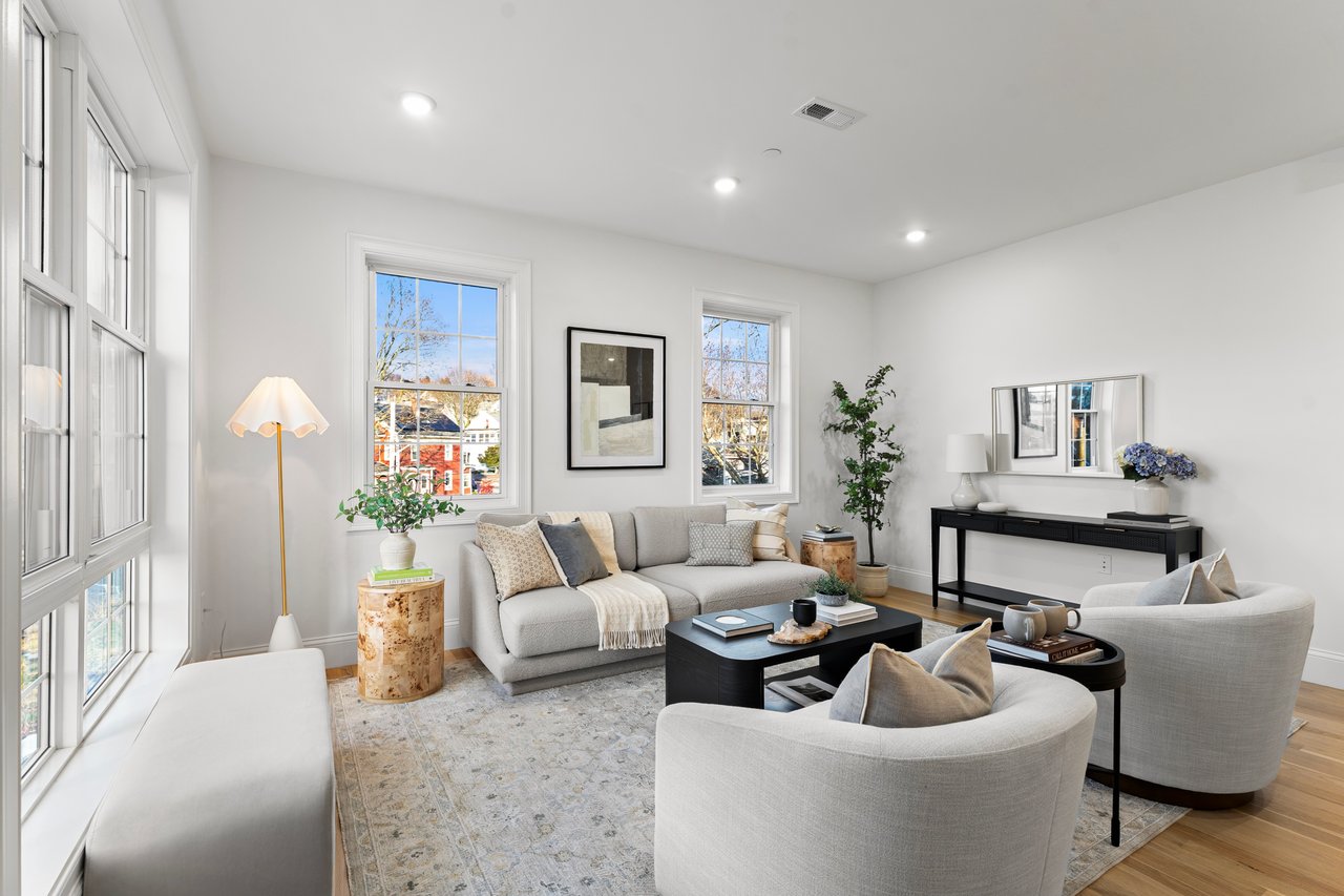 Staged living room with a gray sectional, curved armchairs, and large windows.