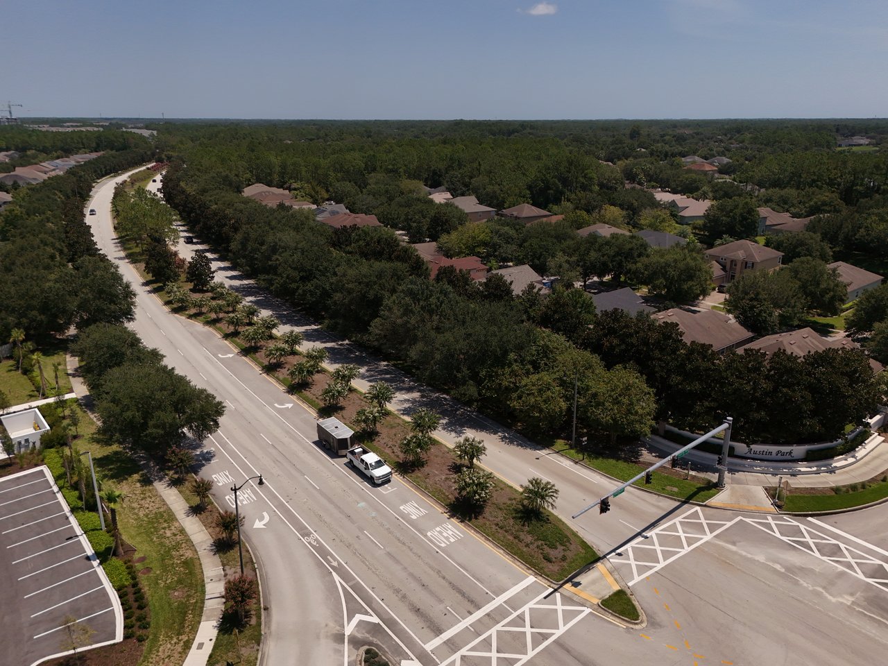 Aerial view of Austin Park homes and tree-lined streets, with the community entrance sign beside an intersection.