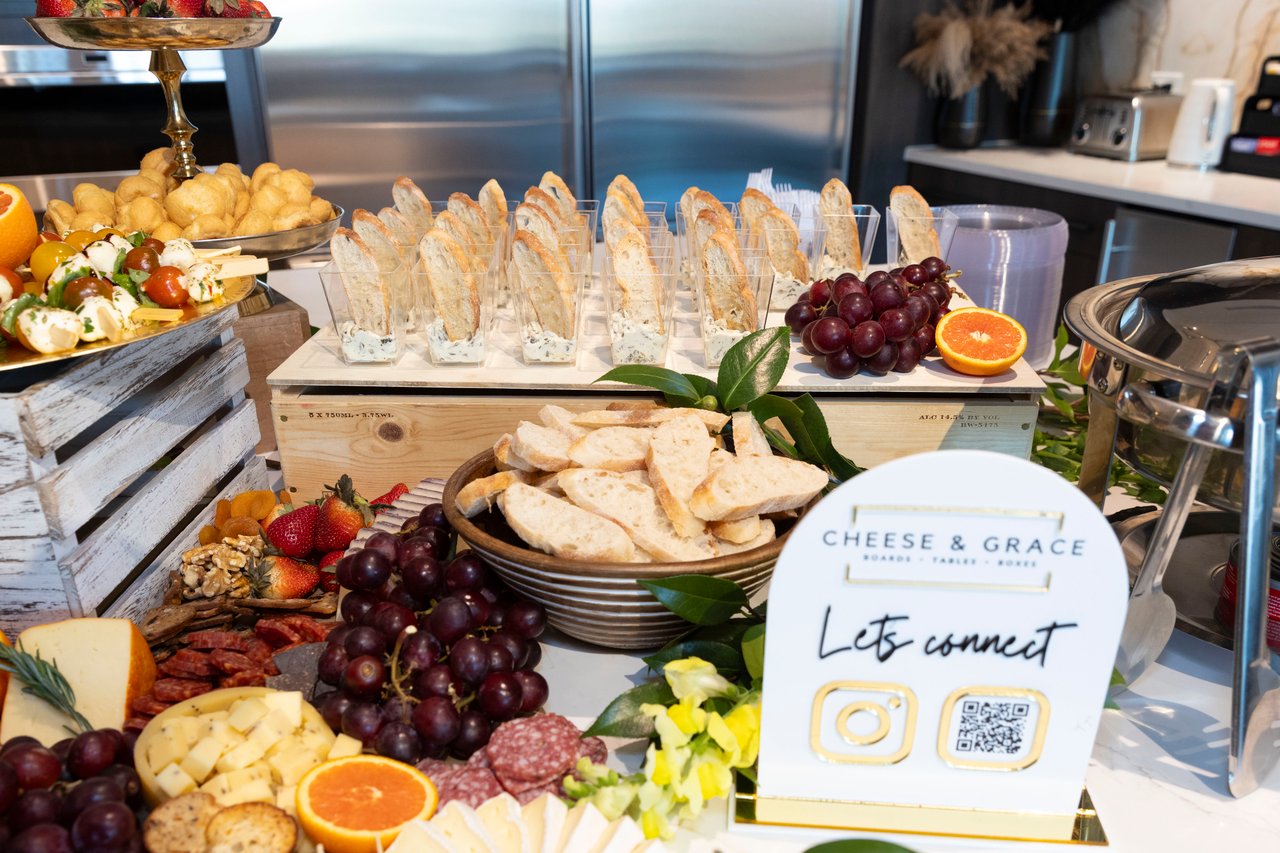 Charcuterie spread with sliced bread, cheese, grapes, fruit, and a Cheese & Grace sign.